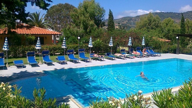 A swimming pool with lounge chairs and umbrellas, surrounded by greenery and a mountain view. - Eucalyptus Apartment 3 (Porto Azzurro)