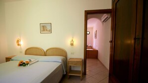A bedroom with a bed, two bedside tables, a nightstand, a wall-mounted picture, and an open door leading to a bathroom. - Eucalyptus Apartment 3 (Porto Azzurro)