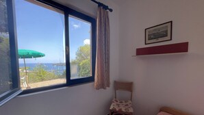 A room with a window, a chair, a bed, a picture on the wall, and a green umbrella outside.