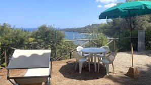 An outdoor seating area with a table and chairs, a green umbrella, and a view of the sea.