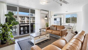 A modern living room with a sofa, coffee table, and a dining area with a table and chairs. - Beachside Apartment (Sunshine Coast)
