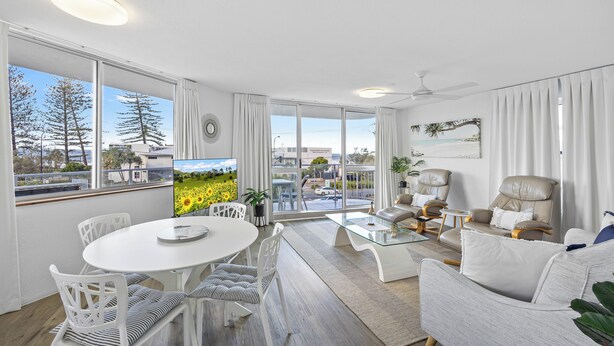A modern living room with a white dining table, white chairs, a glass coffee table, and two leather armchairs. - Beachside Apartment (Sunshine Coast)