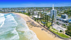 A coastal cityscape with a beach, residential buildings, and a prominent tower. - Beachside Apartment (Sunshine Coast)