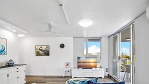 A modern living room with a flat-screen TV, a ceiling fan, and a large window.