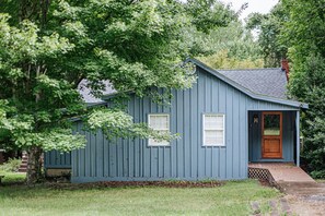 Een klein, gelijkvloers huis met een blauwe gevel, een houten voordeur en een klein terras.