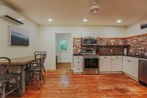 Une cuisine avec un plancher en bois, des armoires blanches, un four à micro-ondes et une cuisinière.