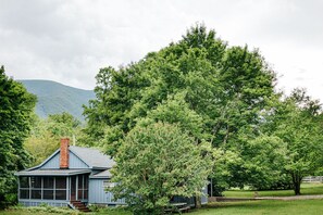 Une petite maison avec un porche et un grand arbre devant.