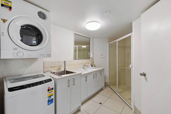 A compact kitchen with a built-in washing machine, a sink, and a glass shower enclosure.