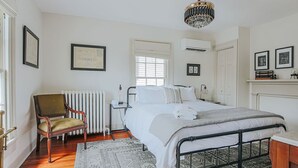 A bedroom with a bed, a chair, a radiator, and a chandelier. - The Woodward: Walk Downtown, Staunton Mural (Staunton)