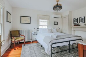 A bedroom with a bed, a chair, a radiator, and a chandelier. - The Woodward: Walk Downtown, Staunton Mural (Staunton)