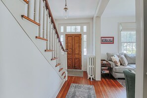 Un escalier avec des rampes blanches et des mains courantes en bois, menant à une porte en bois.