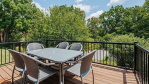 Une terrasse dotée d’une table et de chaises, entourée d’une rambarde, et offrant une vue sur une zone boisée.