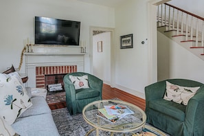 A living room with a fireplace, green armchairs, a sofa, a flat-screen TV, and a staircase.