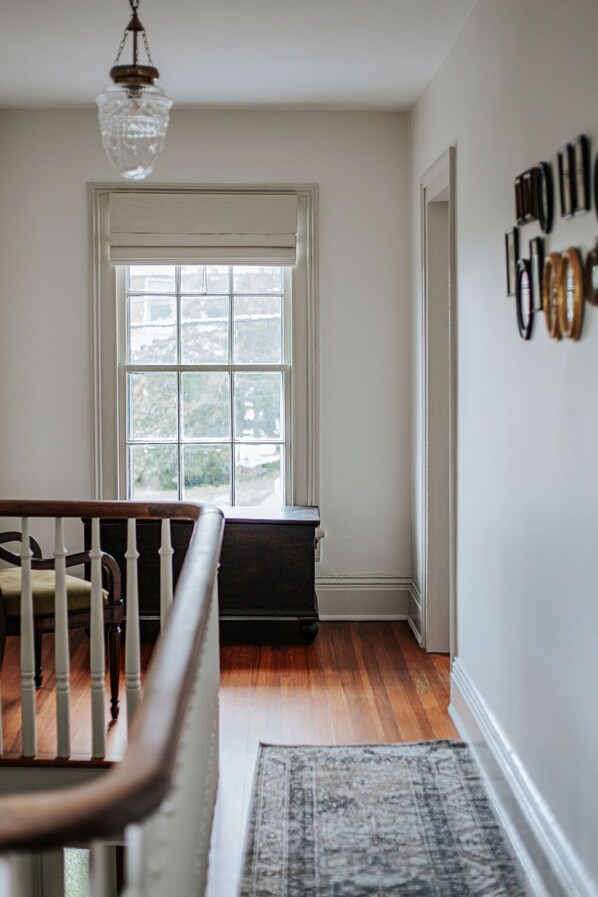A room with a wooden staircase, a large window, a dark piece of furniture, and a patterned rug.