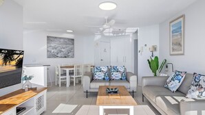 A modern living room with a flat-screen TV, a dining area, and a sofa with floral cushions.