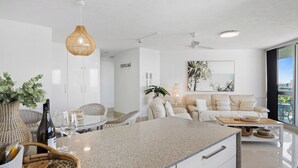 A modern kitchen with a granite countertop, white cabinetry, and a dining area with wicker furniture.