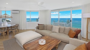 A modern living room with a large sofa, a wooden coffee table, and a dining area with a round table and chairs.