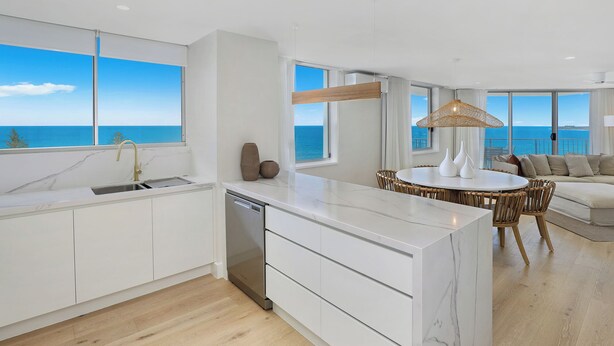 A modern kitchen with a view of the sea, a dining area with a round table, and a living room with a sofa.