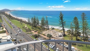 A coastal road with a view of the ocean and beach, surrounded by trees and a park area.