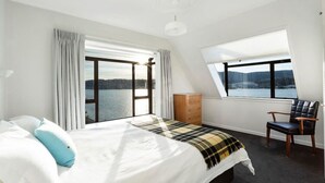 A bedroom with a large bed, a chair, a dresser, and a window with a view of a body of water.