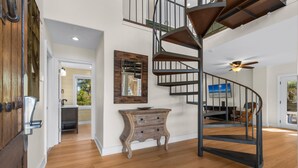 A spacious room with a spiral staircase, wooden flooring, a vintage-style dresser, and a large mirror.