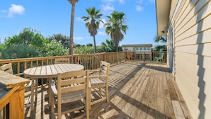 A wooden deck with a table and chairs, surrounded by palm trees and a building.