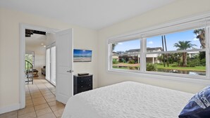 A bedroom with a large bed, a view of a garden, and a door leading to another room.