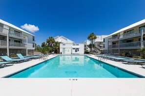 Une piscine avec des chaises longues, un bâtiment doté de balcons et des palmiers.