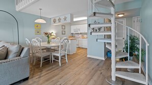 Un vaste espace de vie comprenant une table à manger, des chaises blanches, un canapé et un escalier agrémenté d’un arbre à chat.
