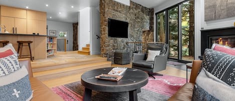 A modern living room with a stone fireplace, a flat-screen TV, and a cozy seating area with a coffee table.