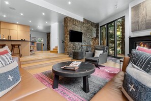 A modern living room with a stone fireplace, a flat-screen TV, and a cozy seating area with a coffee table.