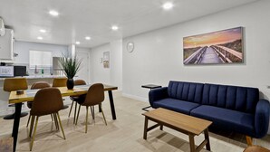 Ein modernes Wohnzimmer mit einem Holzesstisch, braunen Stühlen, einem blauen Sofa und einem Sonnenuntergangsbild an der Wand.