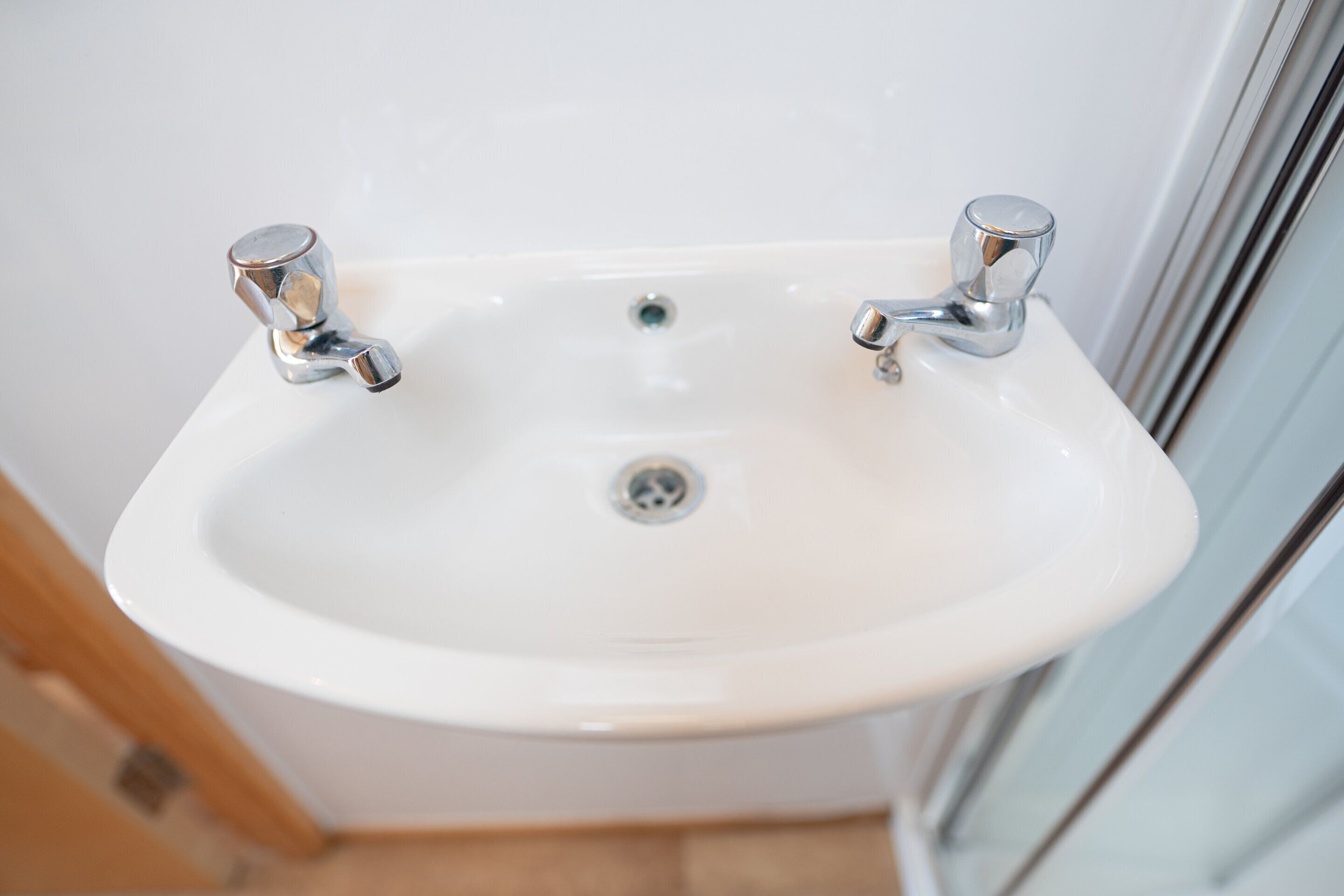 Un lavabo de salle de bain blanc, doté de deux robinets chromés et d’un drain.