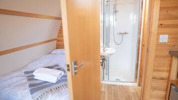 Quarto de cabana de madeira com cama, chuveiro e pia pequena.