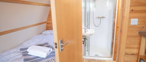 A wooden cabin room with a bed, a shower, and a small sink.