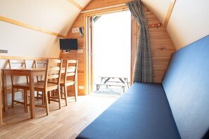 Una habitació petita i acollidora amb una taula i cadires de fusta, un sofà blau i una finestra amb cortines.