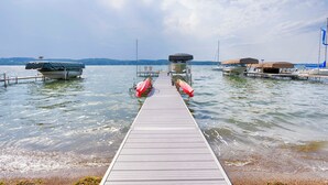 A wooden dock leading to a boat dock with a covered boat and a lifeboat. - Lake Escape: The Definition of Lakefront Luxury (Canandaigua)