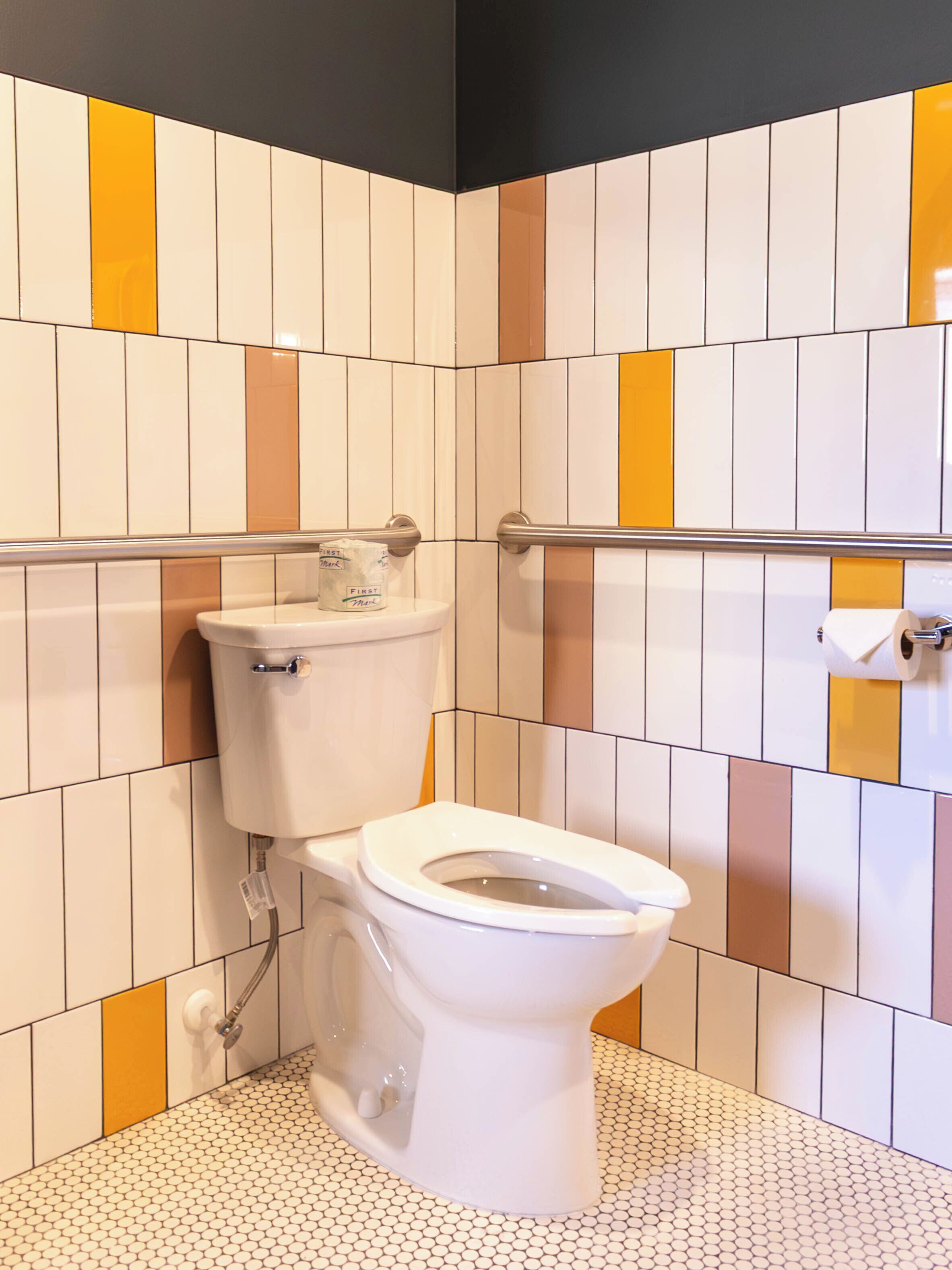 A bathroom with a toilet, a handrail, and a tiled floor.
