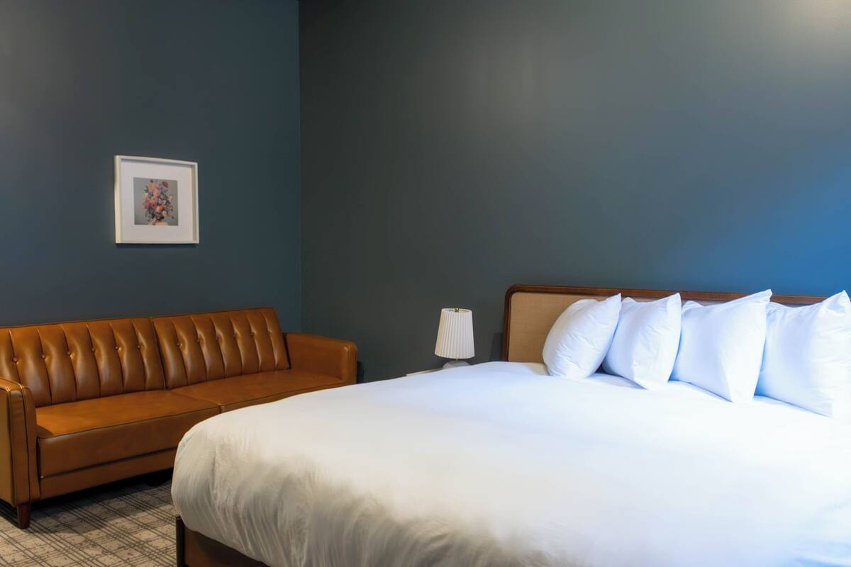 A hotel room with a large bed, a brown leather sofa, a framed picture on the wall, and a bedside lamp.