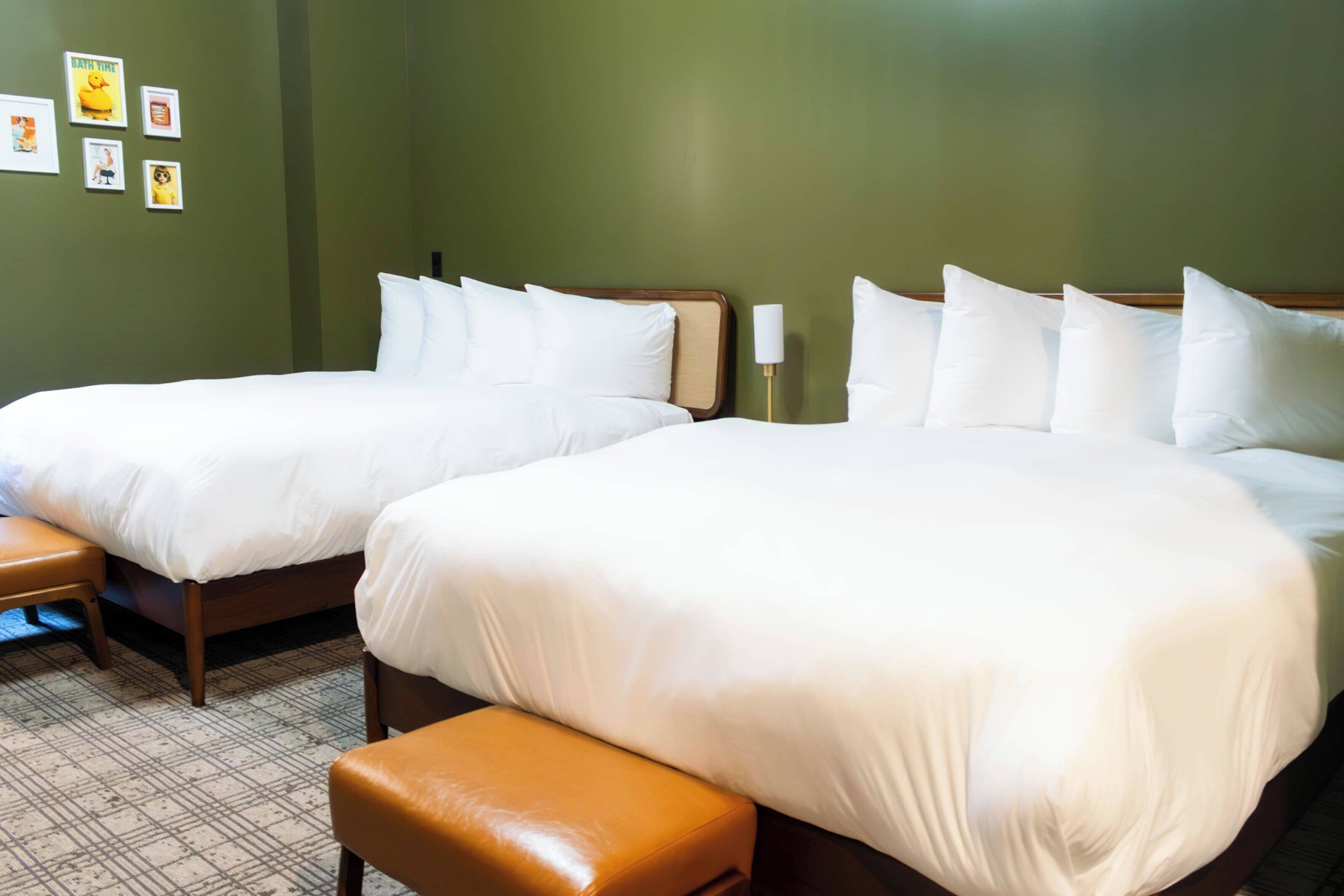 A hotel room with two beds, a bench, and a wall with framed pictures.