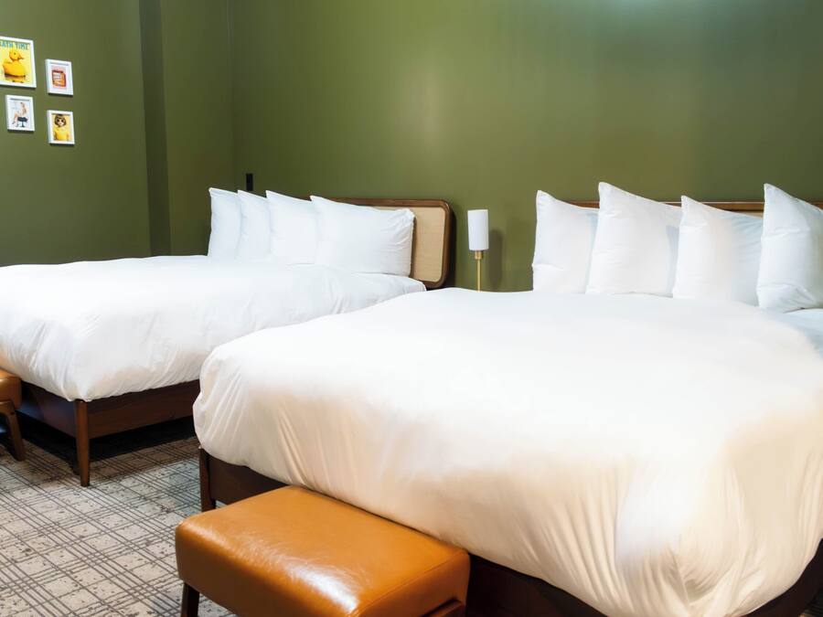 A hotel room with two beds, a bench, and a wall with framed pictures.