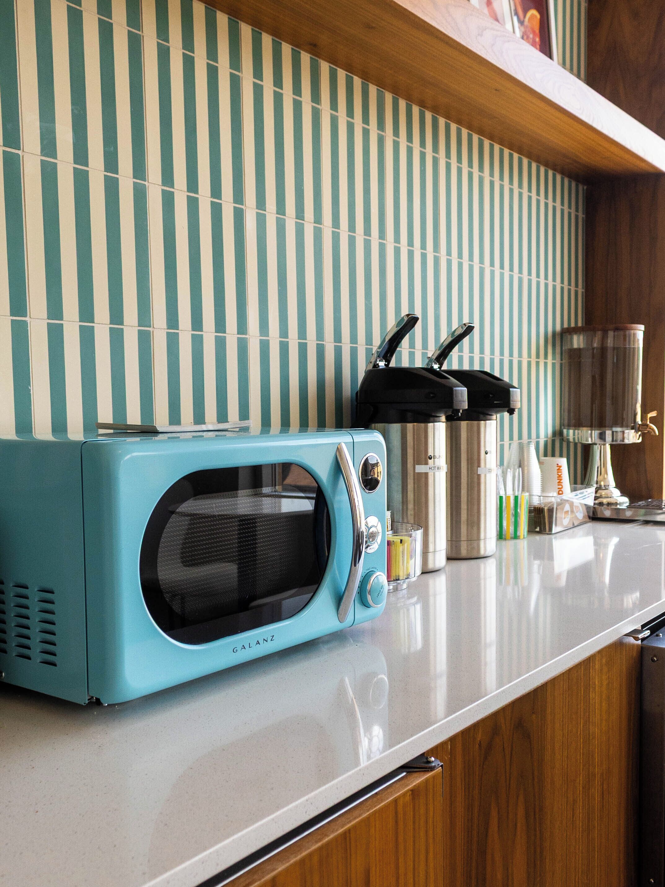 A kitchen with a teal-colored microwave, striped backsplash, and wooden cabinets.