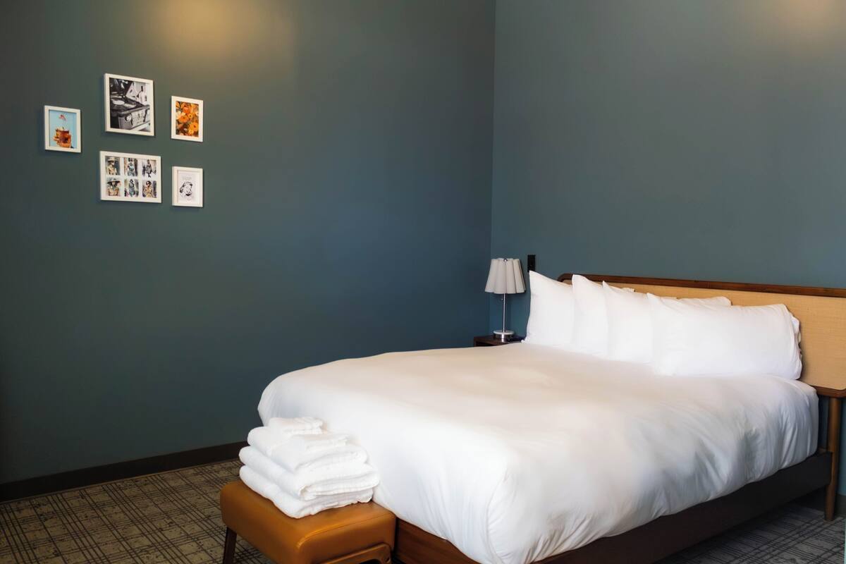 A hotel room with a large bed, a nightstand, a lamp, and wall art.