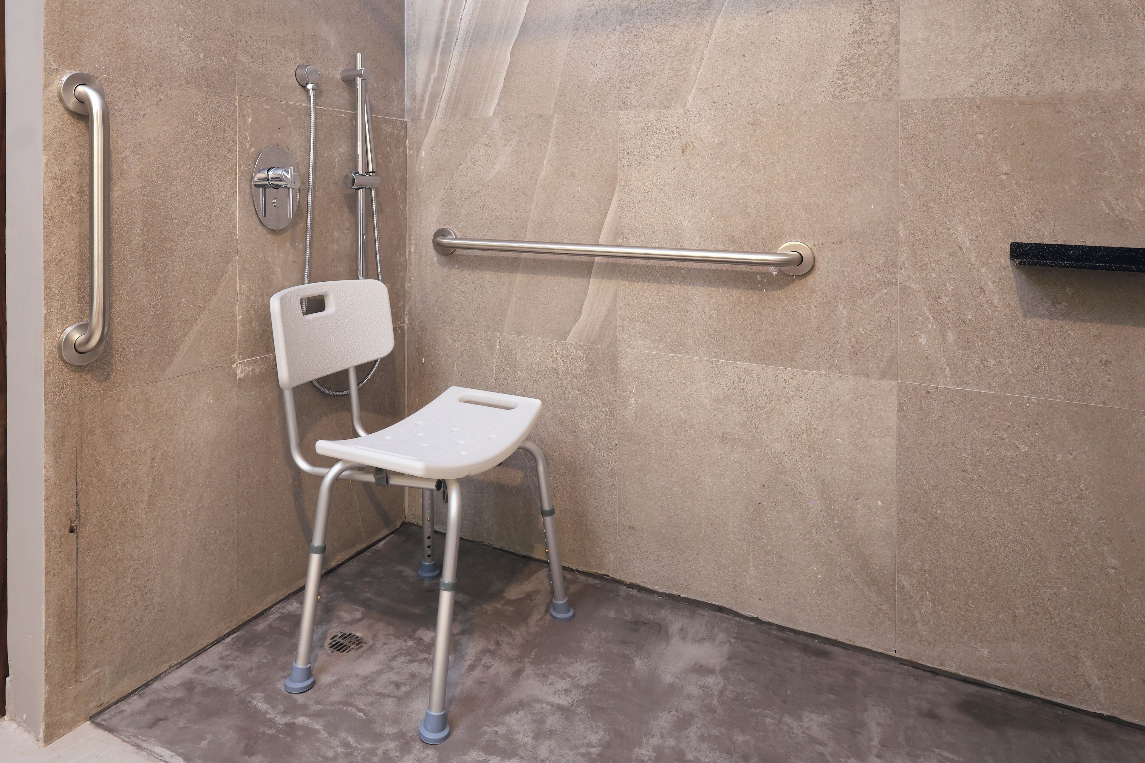 A shower area with a grab bar, a white chair, and a handrail.