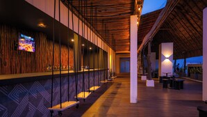 A modern bar area with a TV screen, wooden slatted ceiling, and a series of tables and benches. - Holiday Inn Tulum by IHG (Tulum)