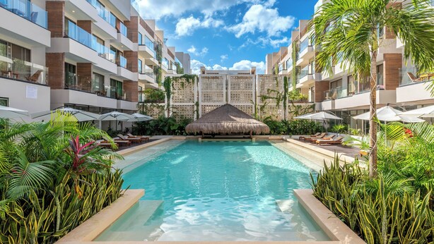 A modern hotel with a central swimming pool surrounded by lush greenery and palm trees. - Holiday Inn Tulum by IHG (Tulum)