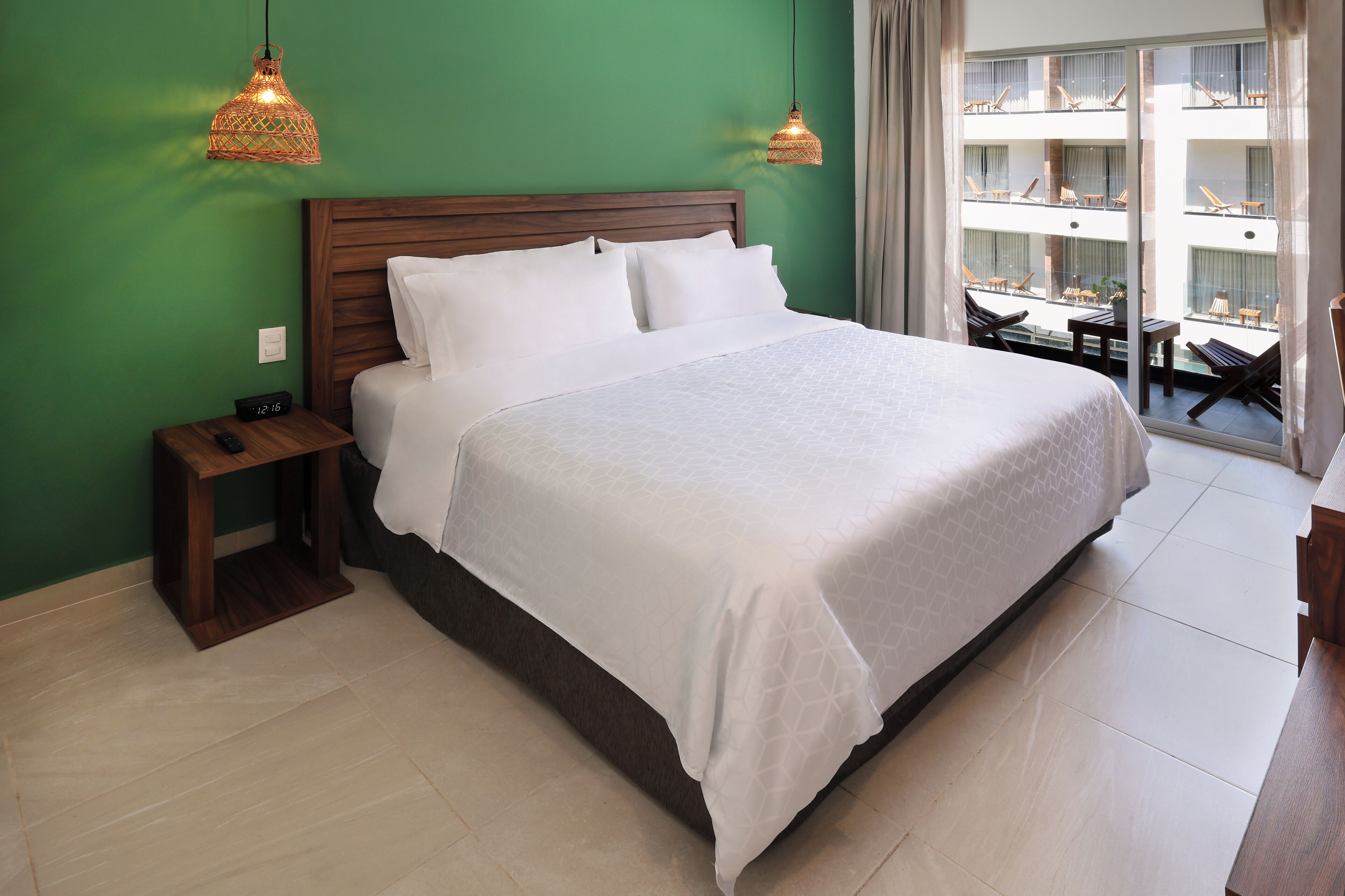 Habitación de hotel con una cama grande, cabecero de madera, dos mesitas de noche y vistas a los balcones del edificio.