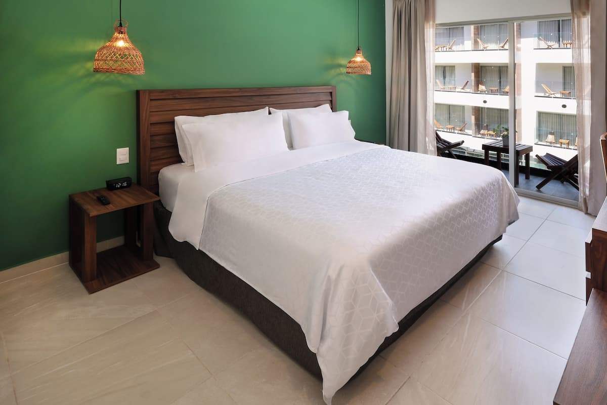 Habitación de hotel con una cama grande, cabecero de madera, dos mesitas de noche y vistas a los balcones del edificio.