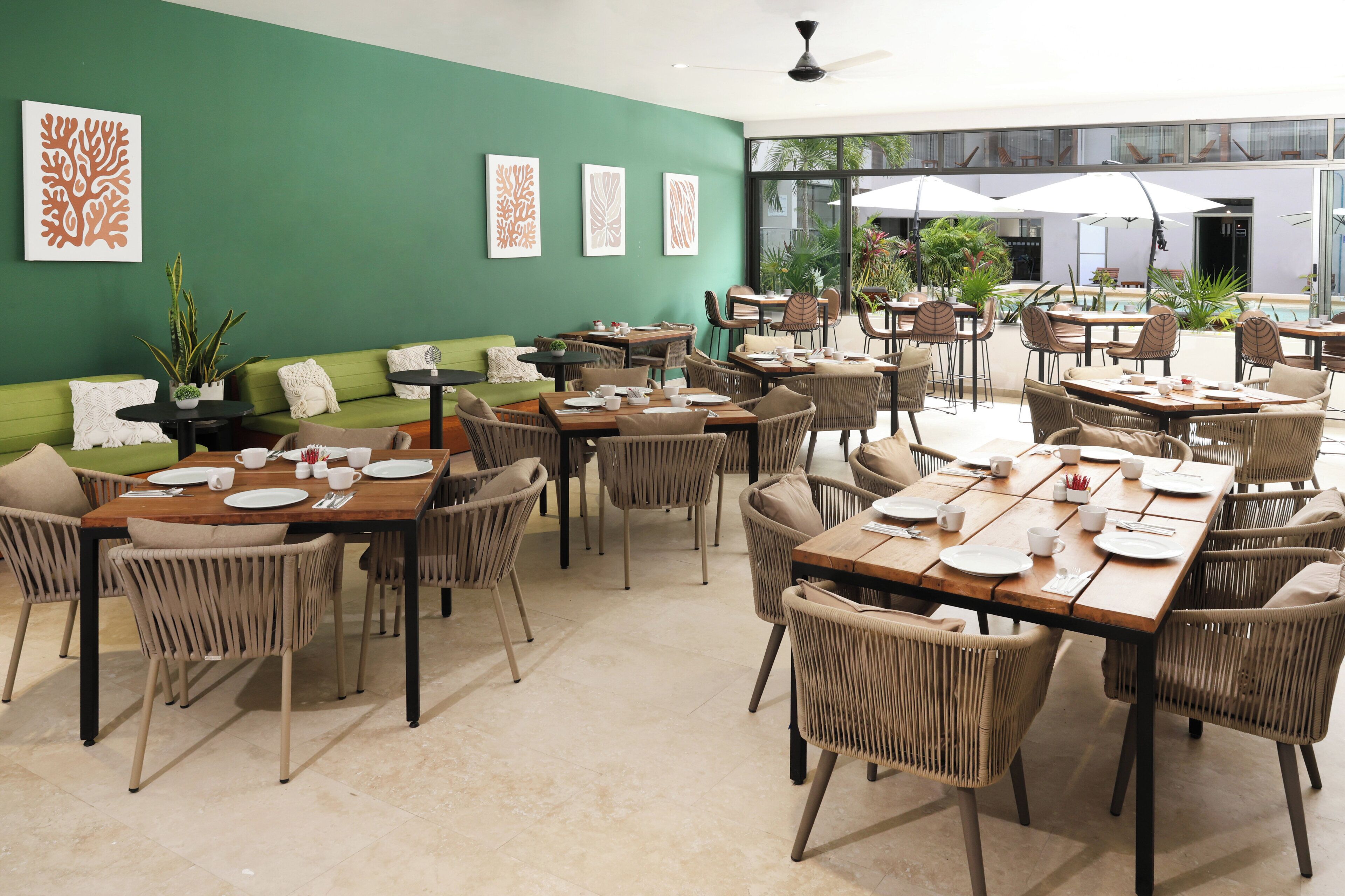 A spacious indoor dining area with multiple tables and chairs, green walls, and framed artwork.