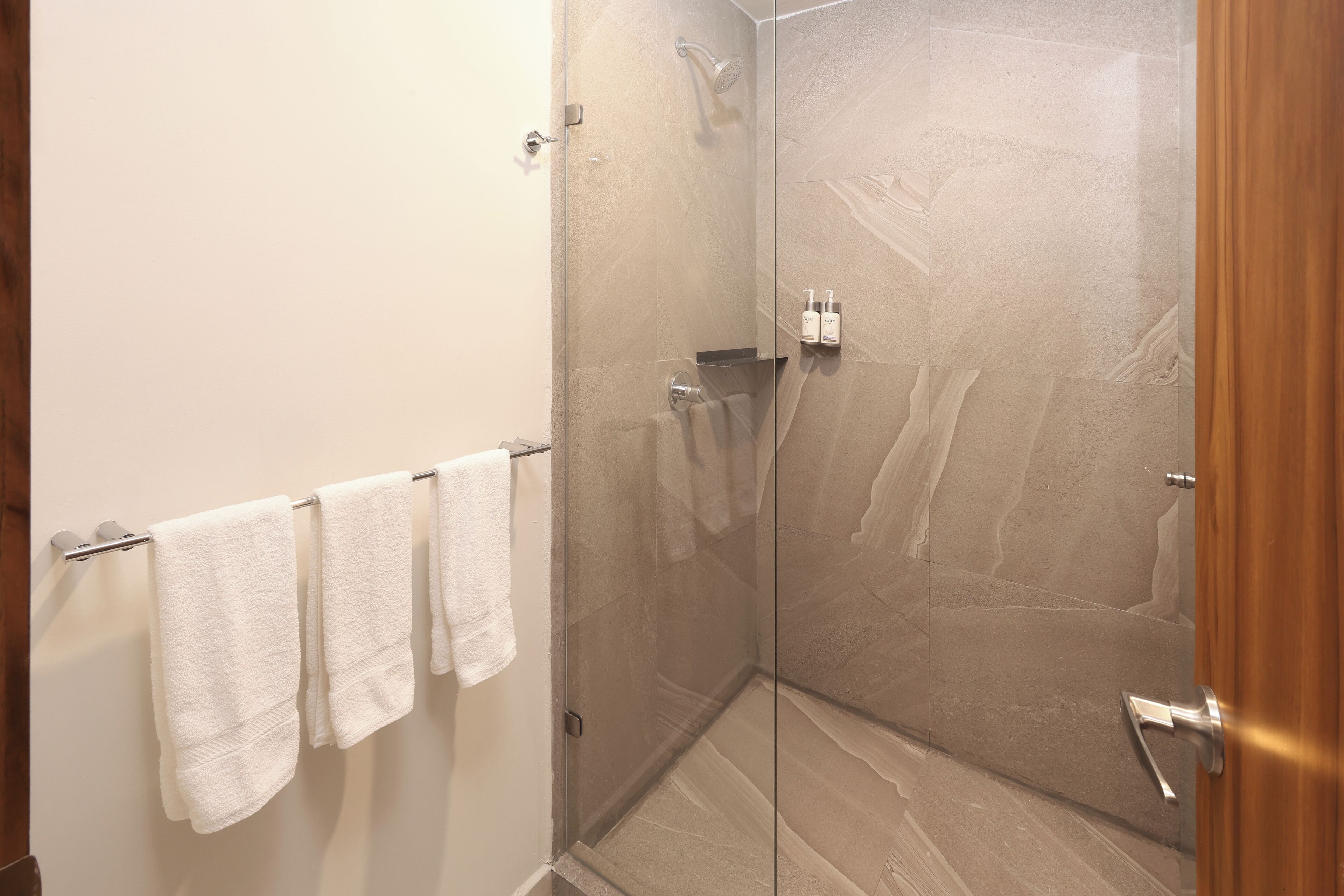 A glass-enclosed shower area with a towel rack and toiletries.